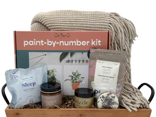 Gift basket with paint-by-number kit, candles, and other items on a white background